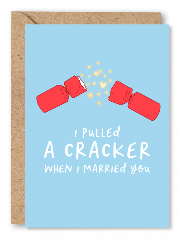 A blue Christmas card featuring an illustration of a pulled crack with hearts and stars exploding from the middle. White text below reads ‘I pulled a cracker when I married you’